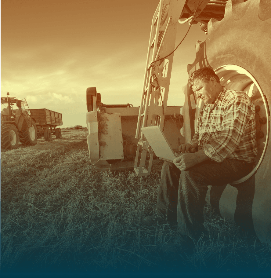 Farmer using a laptop beside a tractor on a field. Technology in agriculture, digital farming, modern farm equipment.