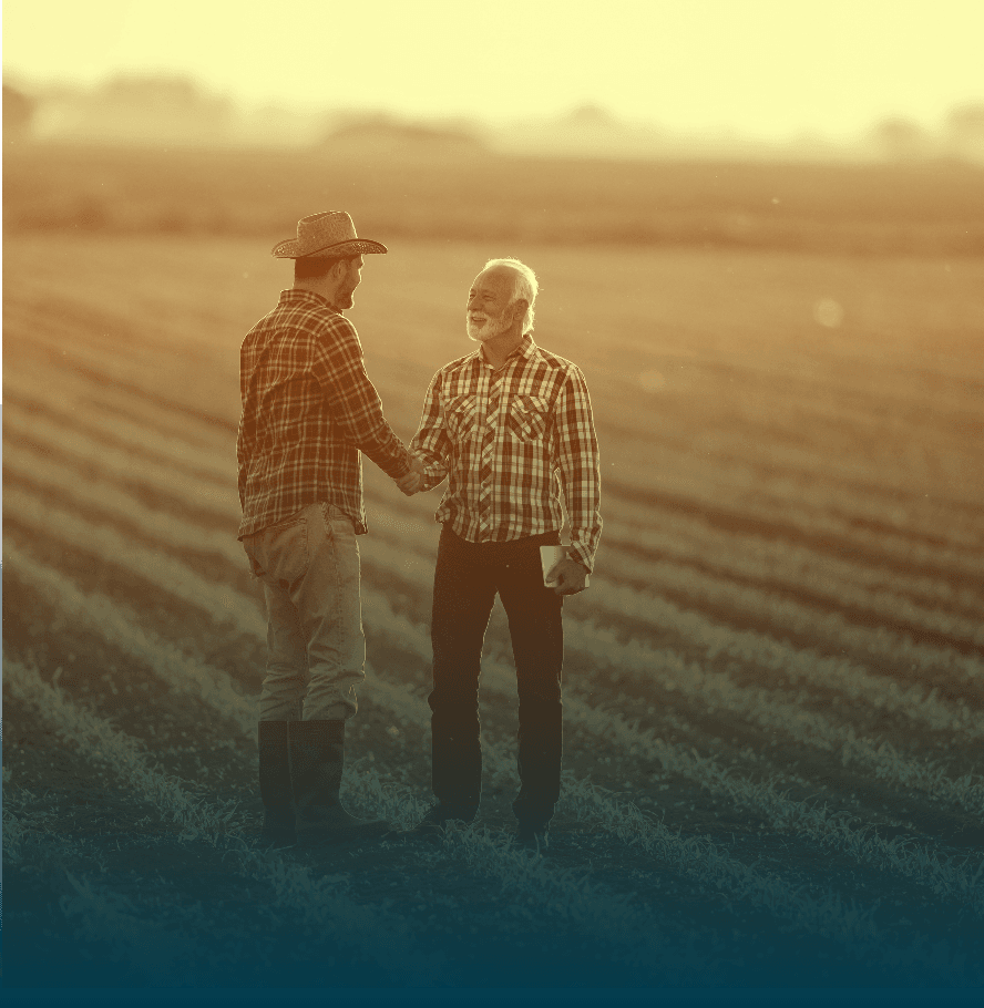 Two farmers in plaid shirts shaking hands in a sunlit field.
